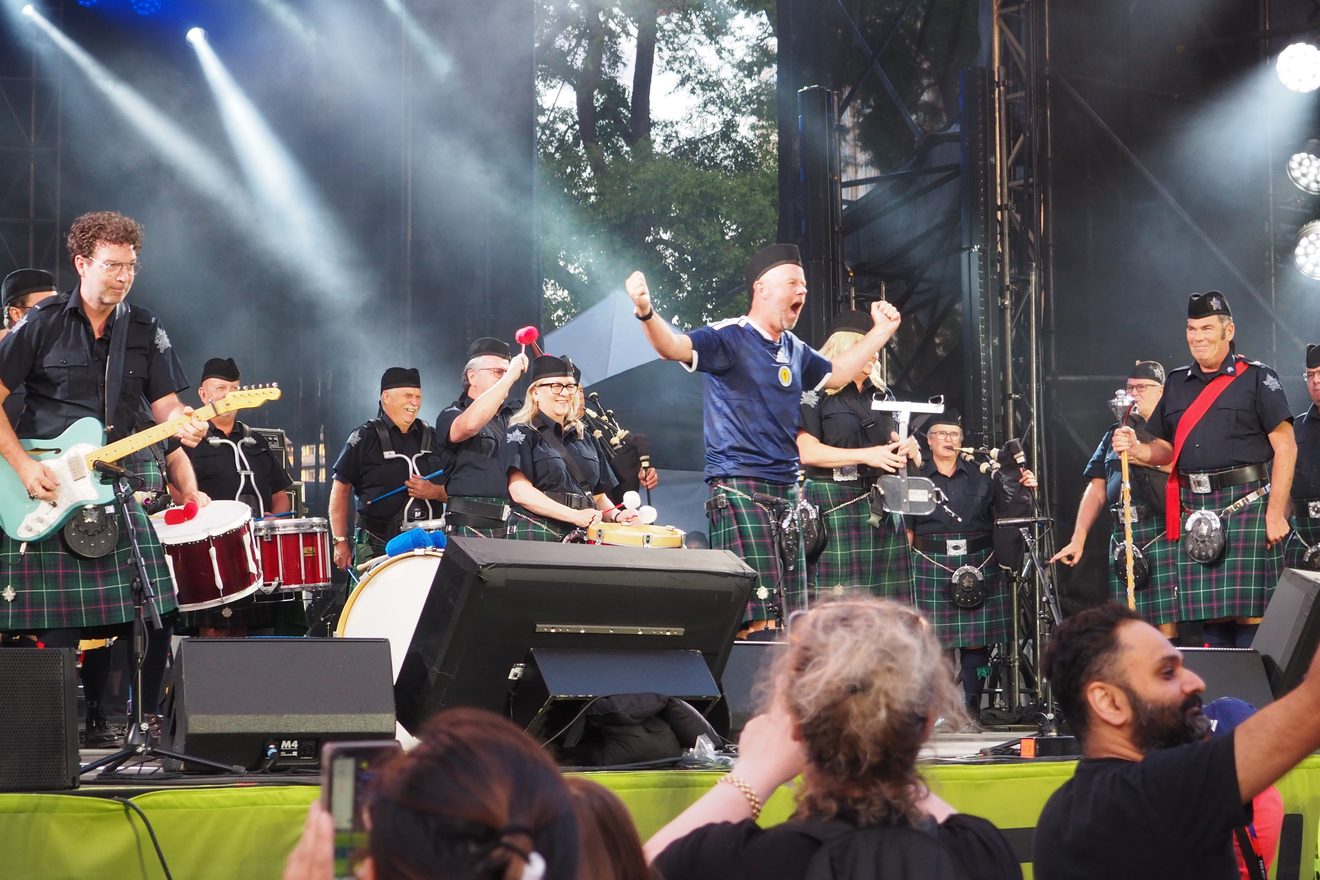 Rich Gordon on a festival stage with the Highland Creek Pipes & Drums, cheering with the band